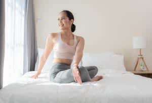 Yoga for Sleep Asian woman doing yoga stretching exercise on bed at home. Morning workout with seated twisting in bedroom. Healthy and sport lifestyle.